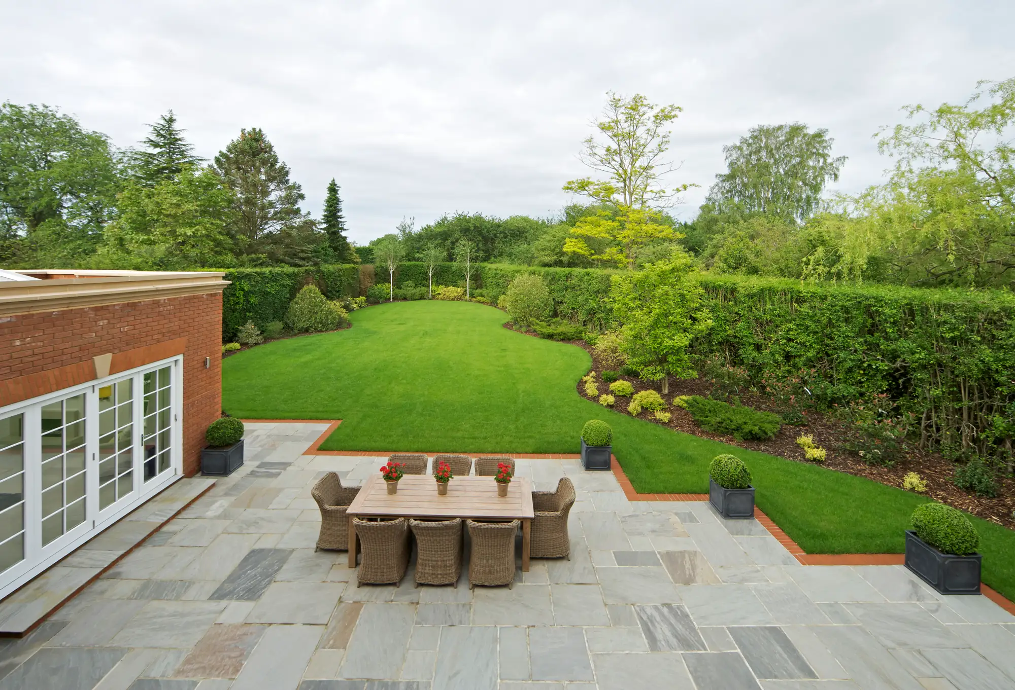 Landscaped garden with a stone patio, dining area and wide lawn