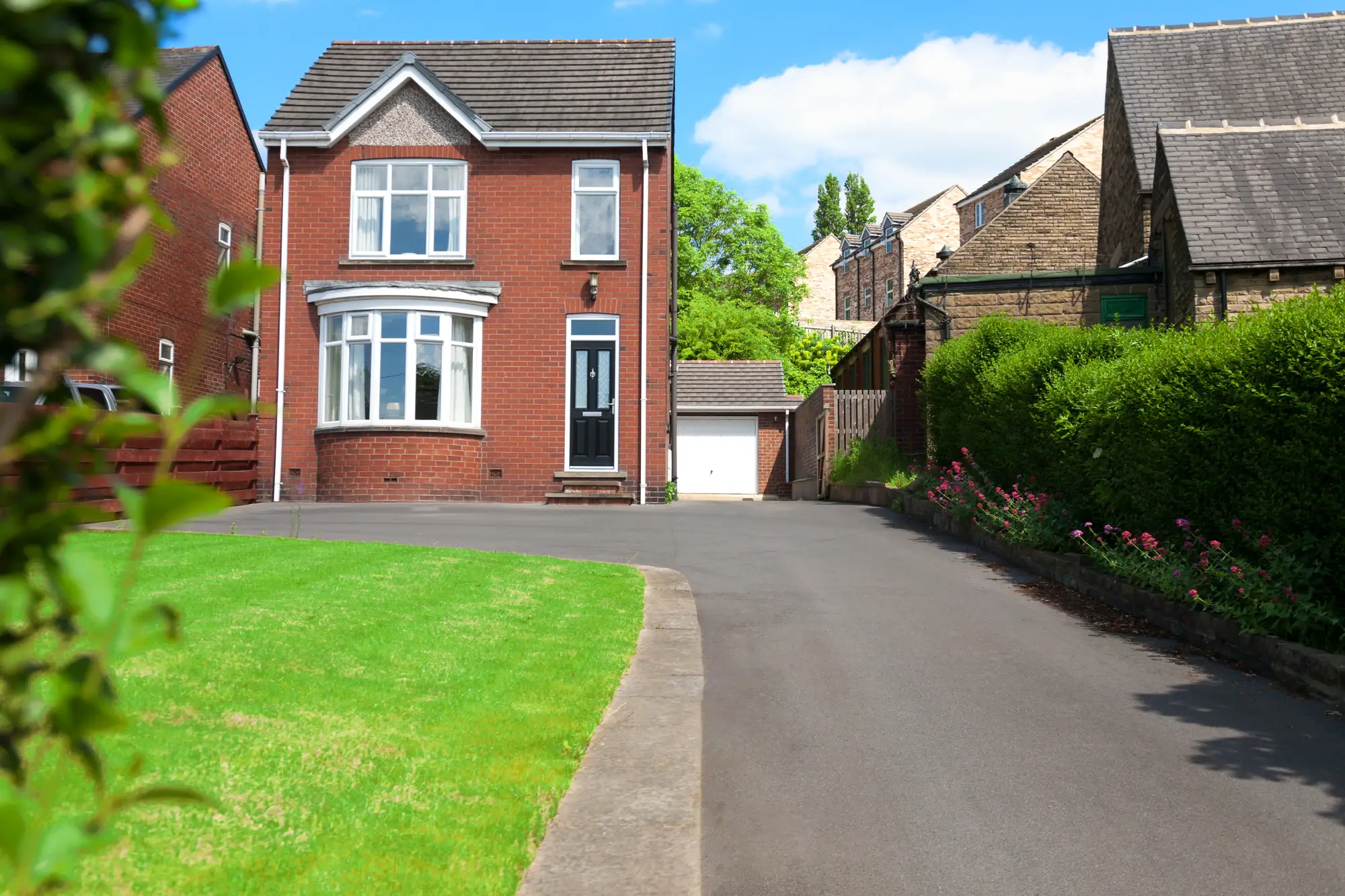 Smooth tarmac driveway curving beside a lawn up to a red brick house